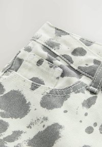Denimstoff mit weißem Hintergrund und großen grauen Spritzmustern. Verfügt über eine Gesäßtasche und sichtbare Nähte.