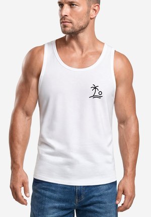 Muskelbepackter Mann, der ein weißes Tanktop mit einem kleinen schwarzen Palmen- und Sonnen-Symbol auf der linken Brust trägt, kombiniert mit blauen Jeans.