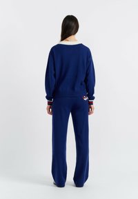Marine gebreid sweater en broek set met een relaxte pasvorm. Bevat gestreepte accenten en een ronde halslijn. Zachte textuur, minimalistisch ontwerp.