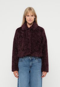 Bordeaux nepbontjas met een kraag, cropped ontwerp en lange mouwen, gecombineerd met vervaagde blauwe high-waisted jeans.