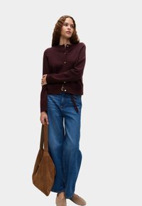 Burgundy cardigan med rund hals och knappstängning, ihopparad med avslappnade blåjeans och en brun mockaväska. Slät tygkvalitet.