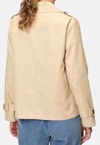 Beige letvægtsjakke med lige skæring, der har knapmanchetter og krave. Glat tekstur, minimal design, velegnet til afslappet brug.