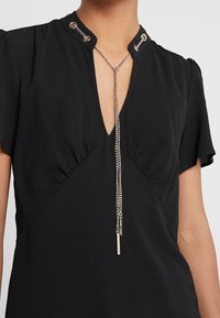 Black blouse with short sleeves, V-neckline, and gathered detailing. Features silver chain accents at collar and hanging charms.