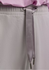 Lichtgrijze stof van de broek heeft een zachte textuur met een geplooide tailleband. Satijnen strik met metallic uiteinden is in het midden van de taille geplaatst.