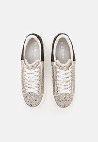 Baskets avec un design argenté et noir, présentant une surface texturée ornée de strass, et des lacets blancs. Logo de la marque visible à l'intérieur.