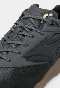 Grey athletic shoe featuring a mixed material upper with mesh and suede textures, flat laces, and a light brown rubber sole.