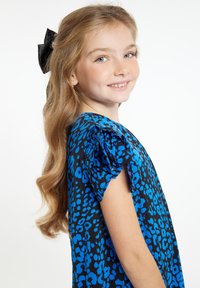 Abito blu con stampa leopardata, maniche a sbuffo corte, sfondo di tessuto nero, texture liscia e un fiocco nero nei capelli mossi.