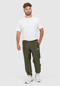 Witte katoenen heren t-shirt met een klein gouden logo, gecombineerd met olijfgroene joggers met elastische tailleband en ritszakken, voorzien van witte branding.