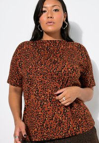 Camiseta de estampado de leopardo marrón con mangas cortas, cuello redondo y una textura suave. Presenta acentos en negro y dorado en el patrón.