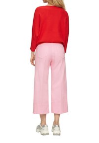 Haut à manches longues rouge côtelé assorti à un pantalon large rose. Le pantalon possède des poches arrière et un ourlet net, complété par des baskets grises.