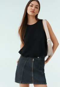 Černý strukturovaný top bez rukávů spárovaný s tmavými džíny sukně s předním zipem. Modelka nese světle béžovou kabelku přes rameno.