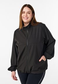 Schwarze Softshell-Jacke mit Reißverschluss, hohem Kragen und elastischen Bündchen. Verfügt über zwei Seitentaschen und ein locker geschnittenes Design.