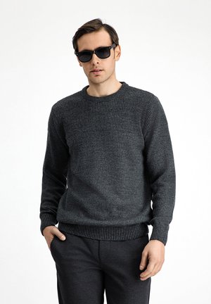 Dark gray knitted sweater with ribbed texture, crew neck, and long sleeves, paired with dark gray pants. Actor wears black sunglasses.
