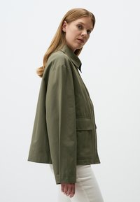 Giacca verde oliva con vestibilità comoda, ampio colletto e tasche laterali. Realizzata in un tessuto morbido e leggero. Presenta un orlo dritto.