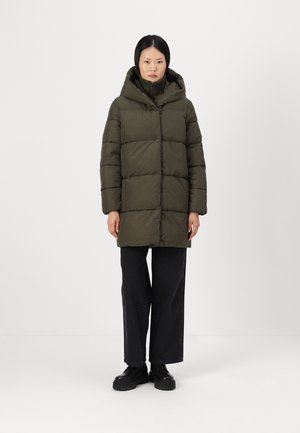 Doudoune en vert olive, avec une capuche, un design matelassé et une fermeture à l'avant. Associée à un jean noir ample et des bottes noires épaisses.