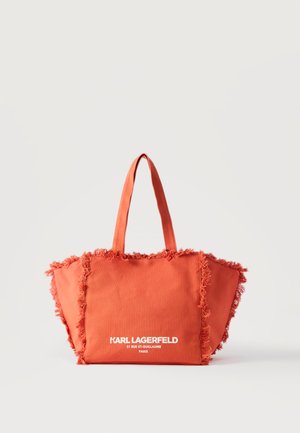 Lys oransje handlenett med frynsete kanter og to håndtak, med hvit tekst "KARL LAGERFELD 21 RUE ST-GUILLAUME PARIS" på frontlommen.