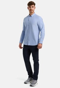 Camicia azzurro chiaro con maniche lunghe, realizzata in cotone, abbinata a pantaloni blu scuro e sneakers grigie. Design semplice con una sottile trama.
