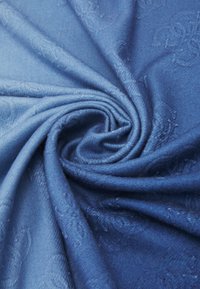 Tejido azul ligero con una textura suave, que presenta un patrón floral en relieve, dispuesto en una formación en espiral.