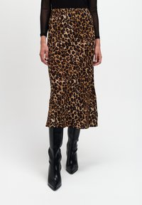 Midi spódnica w prints geparda wykonana z miękkiego materiału, z delikatnym falbanowym wykończeniem u dołu, zestawiona z czarnymi, eleganckimi kozakami do kolan z ostro zakończonym noskiem.