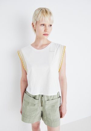 White cotton t-shirt with scalloped yellow and beige sleeve accents, paired with green shorts featuring zip and large pockets.