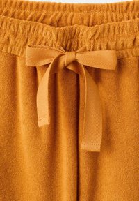 Pomarańczowe spodnie z frotté z elastycznym pasem i zawiązaną płaską tkaninową kokardą z przodu na środku.