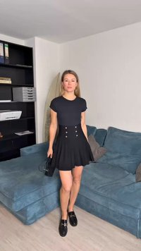 Vestido preto de manga curta com corpete justo e saia rodada, com botões prateados na frente. Usado com sapatos mocassim pretos.