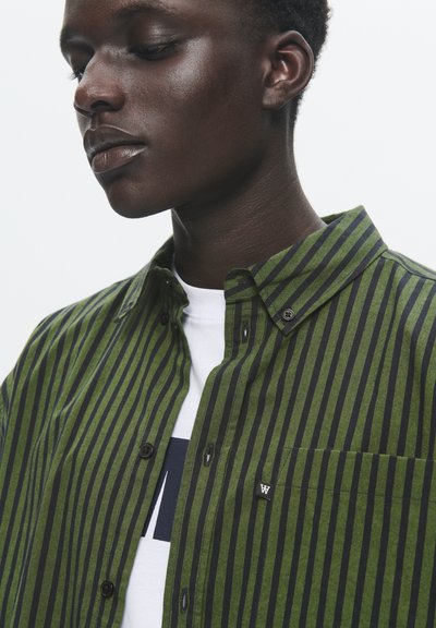 Green and black striped shirt with button-up collar, chest pocket, and logo detail. Made of fabric with a smooth texture.