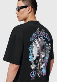 Sort bomulds T-shirt med en farverig grafisk tryk på bagsiden, der skildrer skeletter, blomster og geometriske former. Korte ærmer.
