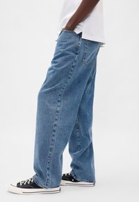 Svetlo modre, široke kavbojke iz jeansa z ravnim krojem, z zadnjimi žepi in šivanimi šivi. Združene s črnimi nizko-top supergami.