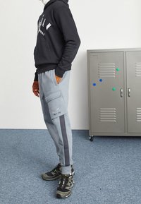Grå sweatpants med sidofickor, mörkgrå ränder och ordet "AIR" i silver. Kombineras med en svart hoodie och löparskor.