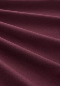 Burgunderfarbener Stoff mit einer glatten Textur, der sanfte Falten und einen dezenten Glanz zeigt, geeignet für Polsterungen oder Kleidungsstücke.