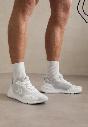 Lichtgrijze sportschoenen van meshstof, met een gewatteerde kraag en een witte rubberen zool. Gepaard met witte geribde sokken, die een gestroomlijnd ontwerp tonen.