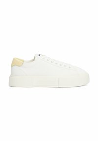Baskets en toile blanches avec une semelle blanche texturée et un onglet de talon jaune pâle, présentant un design à lacets et un logo de marque en relief.