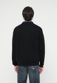 Sweater preto de malha com um corte descontraído, gola redonda e punhos canelados, combinado com jeans azuis desbotados. Design simples, com detalhes mínimos.