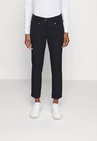 Marinblå byxor med smal passform, med framfickor, metallknappar och uppvikta nederkanter, kombinerat med vita sportskor.