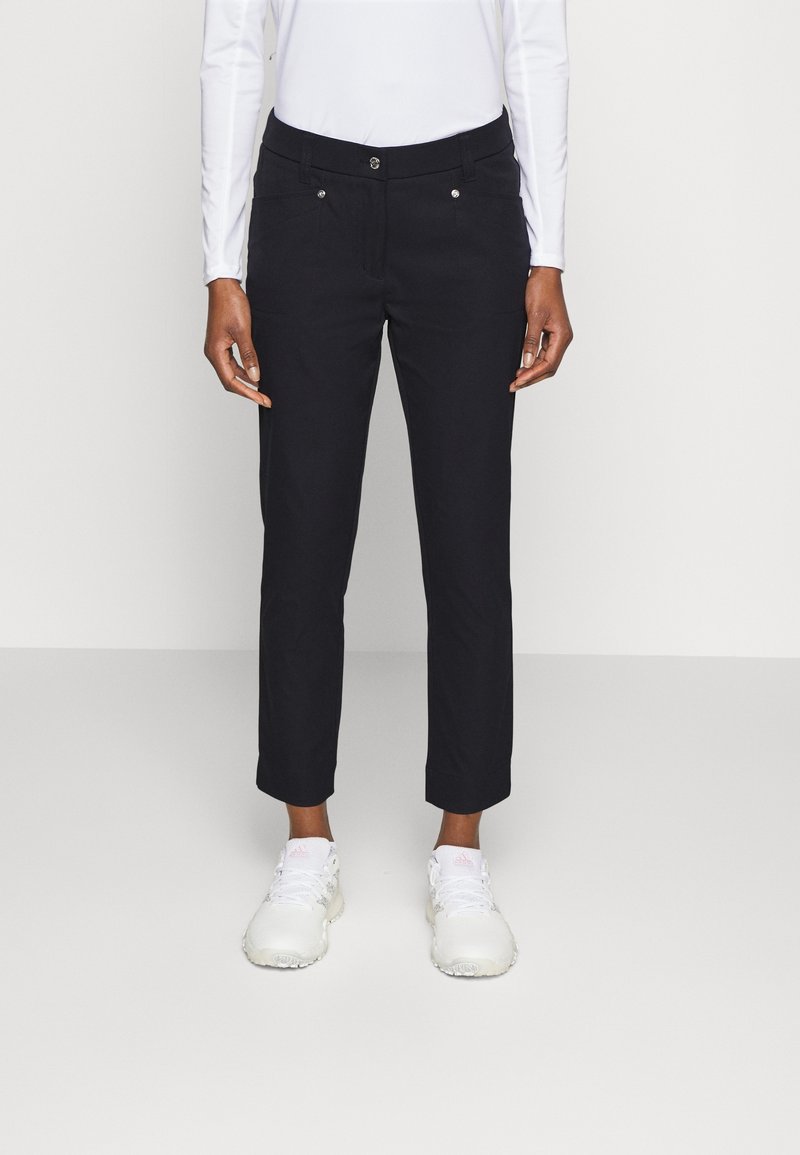 Marinblå byxor med smal passform, med framfickor, metallknappar och uppvikta nederkanter, kombinerat med vita sportskor.