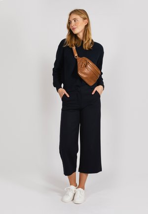 Brun læder crossover taske med et strømlinet design, båret over en marineblå ribbet sweater, parret med vide sorte bukser og hvide sneakers.