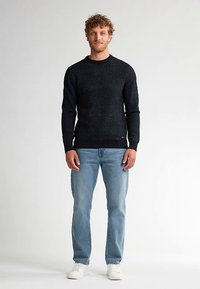 Dunkelblauer, gefleckter Pullover mit rundem Ausschnitt, kombiniert mit hellblauen Jeans und weißen Turnschuhen. Der Stoff wirkt strukturiert und gemütlich.