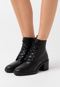 Bottes montantes en cuir noir avec un bout arrondi, dotées d'un lacet à l'avant et d'un talon empilé. La semelle présente un motif antidérapant texturé.