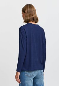 Maglietta a maniche lunghe blu navy con un design in maglia testurizzata, caratterizzata da un collo rotondo e una vestibilità rilassata, abbinata a jeans azzurri chiari.