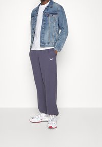 Sininen pesu farkkutakki, rintatasku, valkoinen t-paita, löysät harmaat collegehousut, joissa on Nike-logo, ja valkoiset/punaiset lenkkarit.