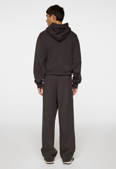 Survêtement gris foncé avec un sweat à capuche et un pantalon ample, fabriqué en tissu doux. Présente des poignets côtelés et une coupe décontractée.