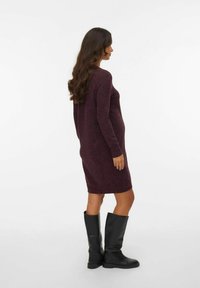 Robe tricotée couleur prune, longueur genou, avec des manches longues. Texture lisse, coupe décontractée et détails sur les coutures latérales. Assortie avec des bottes noires jusqu'aux genoux.