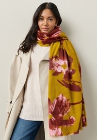 Mustardkollane lillemustriga sall roosade ja burgundia toonidega, valmistatud pehmest kangast, sobitatud heledat beeži kampsuni ja mantliga.