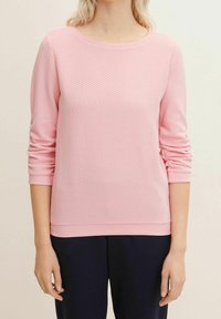 Ljusrosa tröja med ett texturerat mönster, rund halsringning och trekvartslånga ärmar. Har en ribbad nederkant och detaljer på ärmsluten.