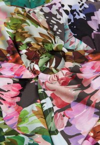 Blumenstoff mit großen rosa, lila und grünen Blumen auf einem dunkelbraunen Hintergrund, mit gerafftem Elastik und einem Meterring-Detail.