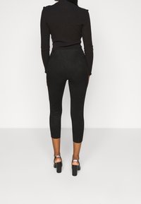 Svart ribbad långärmad topp tillsammans med högmidjade svarta leggings. Leggingsen har en slät textur och räcker till mitten av vaden, bärs med klumpiga klackar.