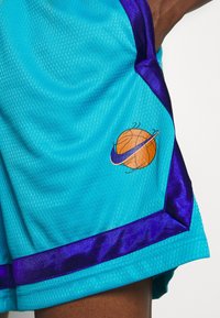 Tyrkysové basketbalové šortky z texturované síťované látky, s fialovým saténovým lemem a logem basketbalového míče s cívkou.