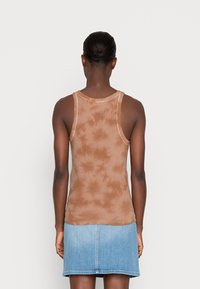 Brun tie-dye linne med ribbad textur och rund halsringning, matchat med en denimkjol. Bakvy visar tröjans design.