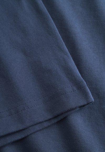 Gros plan sur un tissu en coton bleu marine avec des coutures visibles sur les bords pliés, montrant la texture et les détails des coutures.